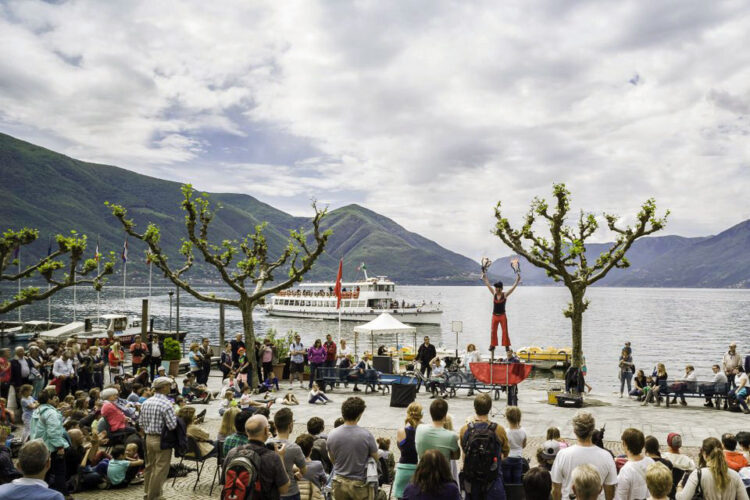 Lungolago di Ascona, artista di strada si esibisce in pubblico. Sullo sfondo, un battello sfond